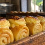 Best Piononos de Santa Fe Near Me, A close-up row of authentic Piononos de Santa Fe, featuring syrup-soaked rolled sponge cake topped with toasted cream, displayed in a traditional Spanish bakery tray.