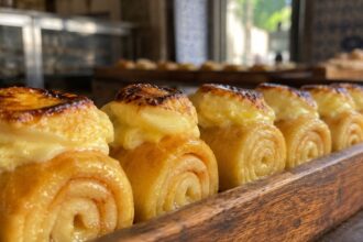 Best Piononos de Santa Fe Near Me, A close-up row of authentic Piononos de Santa Fe, featuring syrup-soaked rolled sponge cake topped with toasted cream, displayed in a traditional Spanish bakery tray.