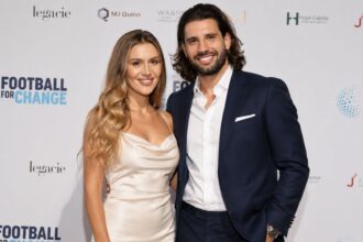 Borka Buzsik, wearing an elegant cream dress, standing alongside her husband, Liverpool footballer Dominik Szoboszlai, who is wearing a navy blue suit at a charity event.