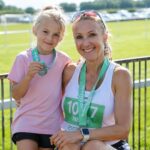 Former marathon runner Paula Radcliffe smiling alongside her daughter Isla Lough, both wearing race bibs and medals after a running event.
