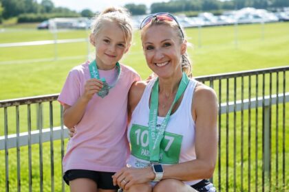 Former marathon runner Paula Radcliffe smiling alongside her daughter Isla Lough, both wearing race bibs and medals after a running event.