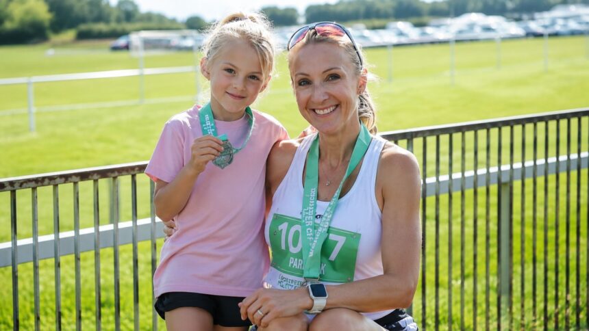 Former marathon runner Paula Radcliffe smiling alongside her daughter Isla Lough, both wearing race bibs and medals after a running event.