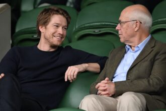 Joe Alwyn in conversation with an older companion at Wimbledon