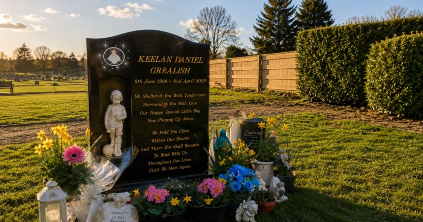 The black memorial headstone of Keelan Daniel Grealish, surrounded by bright flowers, tributes, and a small statue of a boy holding a football in a peaceful cemetery setting.