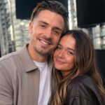 Manchester City footballer Jack Grealish smiling warmly while posing closely with his younger sister Kiera Grealish outdoors against a modern city background.