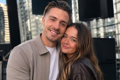 Manchester City footballer Jack Grealish smiling warmly while posing closely with his younger sister Kiera Grealish outdoors against a modern city background.