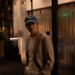 Man in tan blazer and blue LA cap outside a restaurant at night