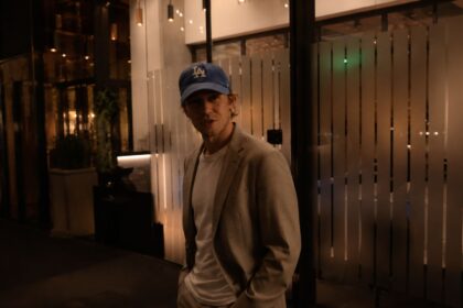 Man in tan blazer and blue LA cap outside a restaurant at night