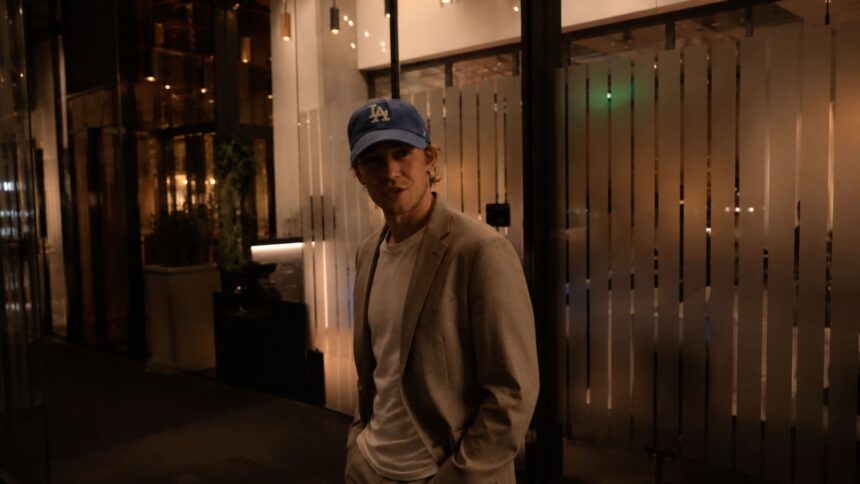 Man in tan blazer and blue LA cap outside a restaurant at night