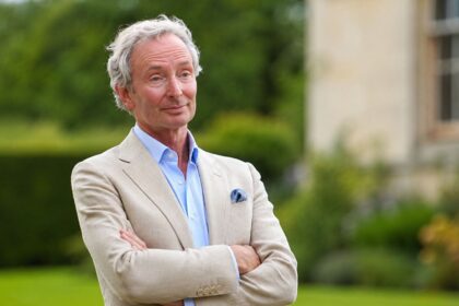 A portrait of Nigel Mackintosh, father of Millie Mackintosh, wearing a beige blazer and light blue shirt in a garden setting.