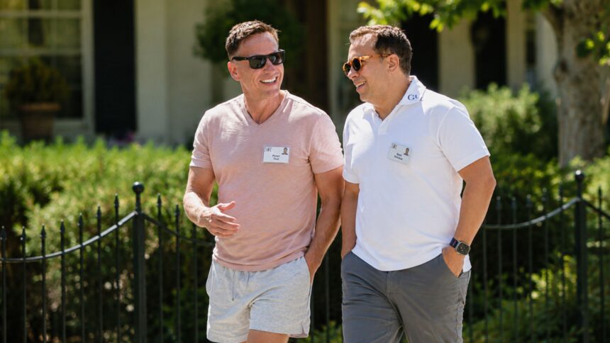 Peter Thiel, wearing a pink t-shirt, and his husband Matt Danzeisen, in a white polo shirt, smiling and talking while walking together outdoors at a conference.