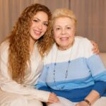 Global music star Shakira sitting affectionately on a couch with her mother, Nidia del Carmen Ripoll Torrado, both smiling warmly at the camera.