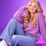 Social media creator and TLC reality star Baylen Dupree smiling warmly while sitting on the floor in a purple sweater and blue jeans against a vibrant purple background.