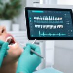 Dental hygienist performing a periodontal exam while an AI voice-charting screen displays real-time tooth charting and audio waveform