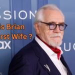 Scottish actor Brian Cox wearing a navy suit and glasses on a red carpet, with text asking "Who is Brian Cox's First Wife?" overlaying the image.