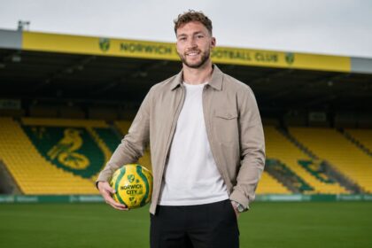 Norwich City right-back Jack Stacey standing on the pitch at Carrow Road holding a yellow and green football.