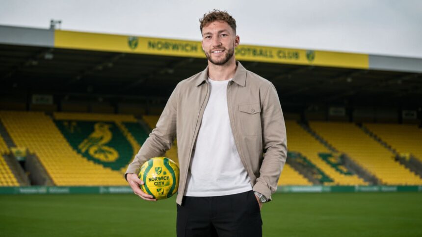 Norwich City right-back Jack Stacey standing on the pitch at Carrow Road holding a yellow and green football.