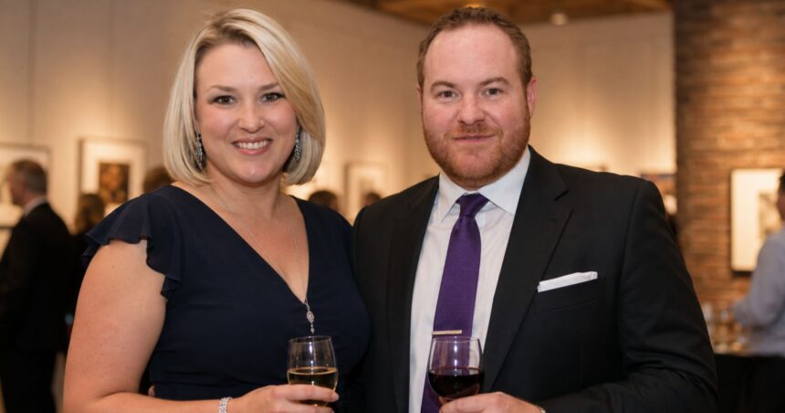 British entrepreneur Sara Davies, wearing a navy blue dress, smiling beside her husband Simon Davies, who is wearing a dark suit and purple tie, at an evening event.