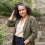 Outdoor editorial portrait of a woman with curly salt-and-pepper hair wearing an olive blazer