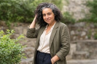 Outdoor editorial portrait of a woman with curly salt-and-pepper hair wearing an olive blazer